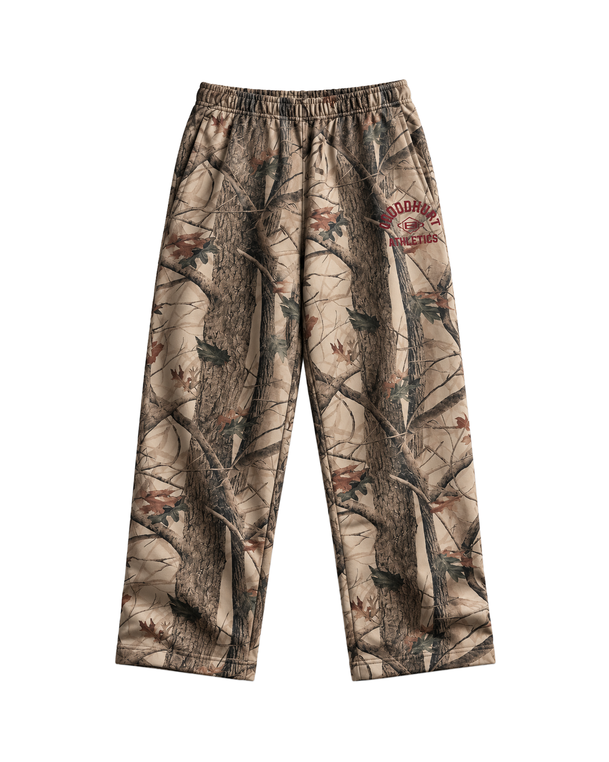 A pair of camouflage pants featuring a realistic tree bark and leaf pattern in shades of brown, beige, and gray, with a 'GOOD HURT' Athletics logo on the upper right leg.