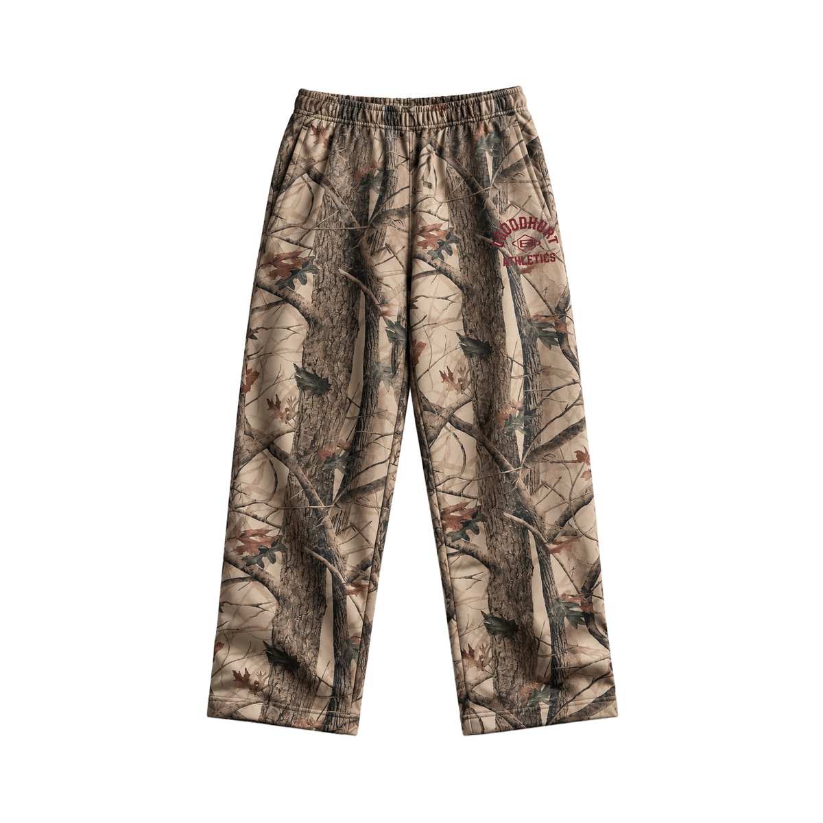 A pair of camouflage pants featuring a realistic tree bark and leaf pattern in shades of brown, beige, and gray, with a 'GOOD HURT' Athletics logo on the upper right leg.