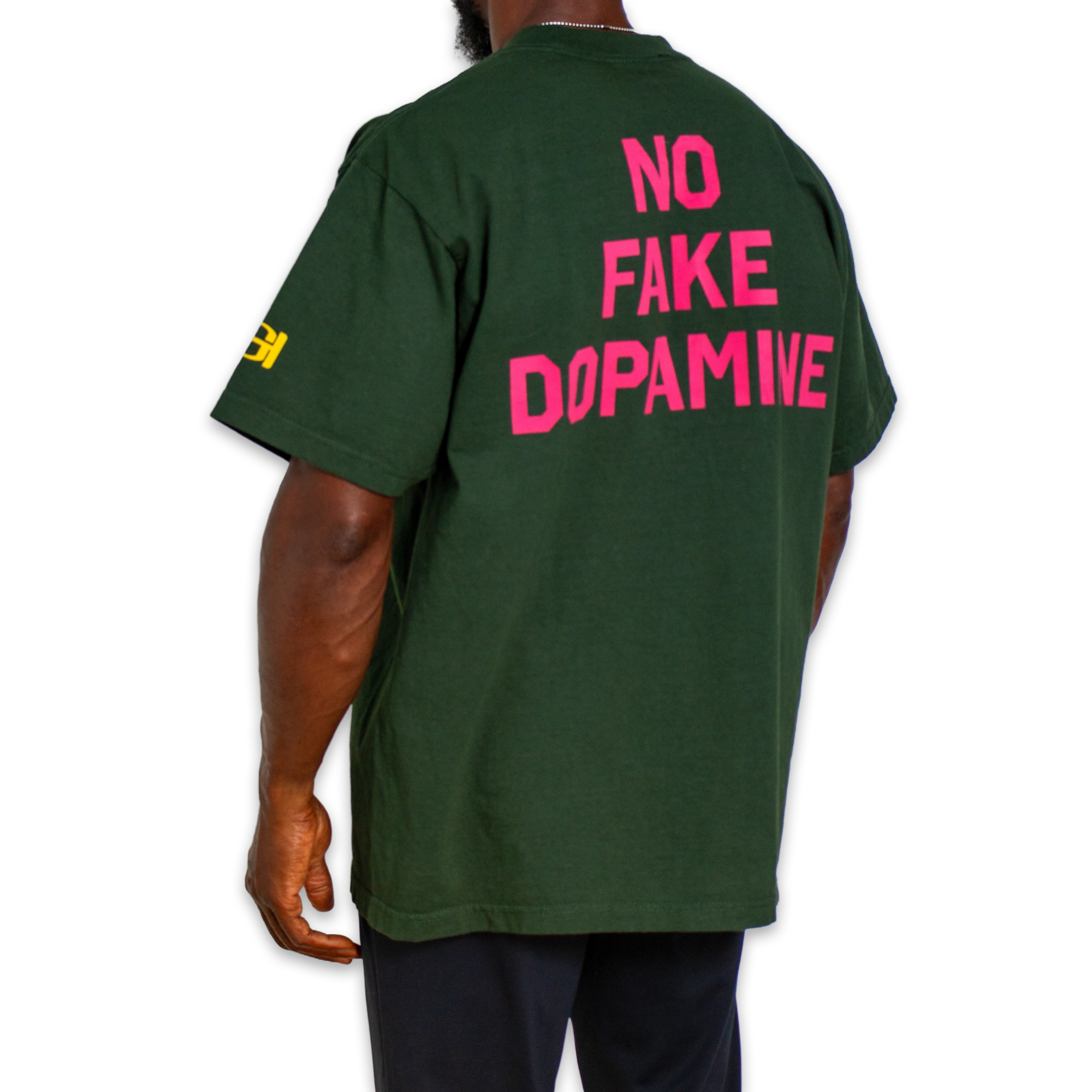 A man wearing a dark green t-shirt from the back, featuring the text 'NO FAKE DOPAMINE' printed in bright pink across the back, with a small yellow graphic on the left sleeve.