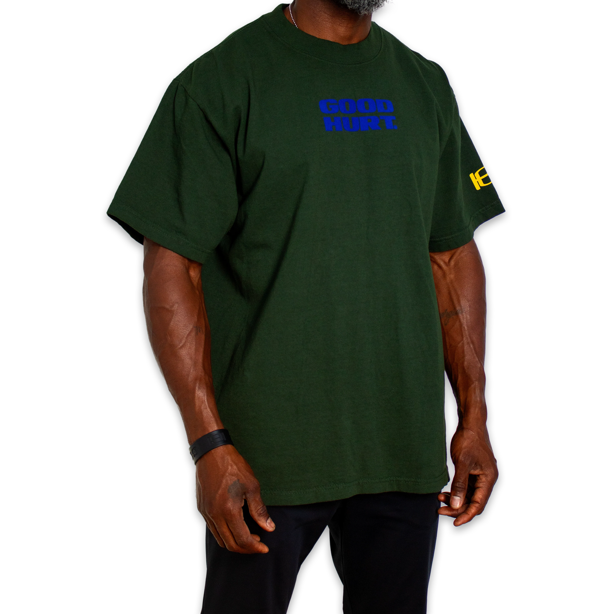 A dark green short-sleeve t-shirt with 'GOOD HURT' printed in blue on the chest and a yellow graphic on the right sleeve, shown on a model against a white background.