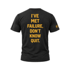 A heather black t-shirt shown from the back, featuring the motivational quote 'I'VE MET FAILURE, DON'T KNOW QUIT.' printed in bold yellow capital letters.
